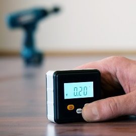 Hand,Holding,A,Small,Digital,Spirit,Level,On,Parquet,Floor.